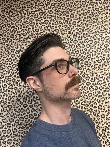 Man with glasses and moustache against leopard print wall.