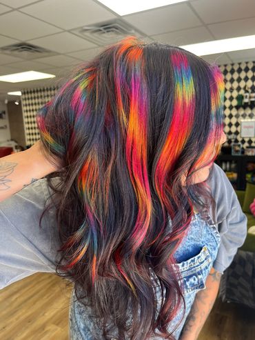 Vibrant rainbow highlights on dark wavy hair.