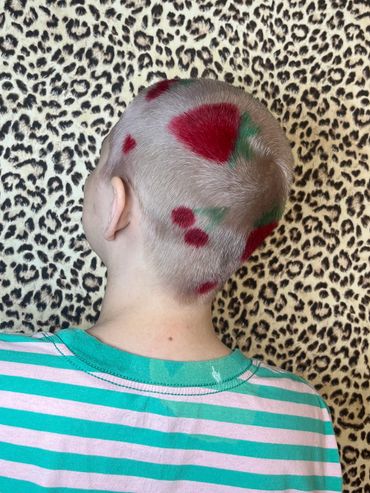 Person with shaved head and colorful hair designs against leopard print background.