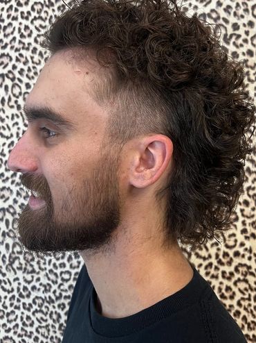 Man with curly mullet hairstyle against leopard print background.