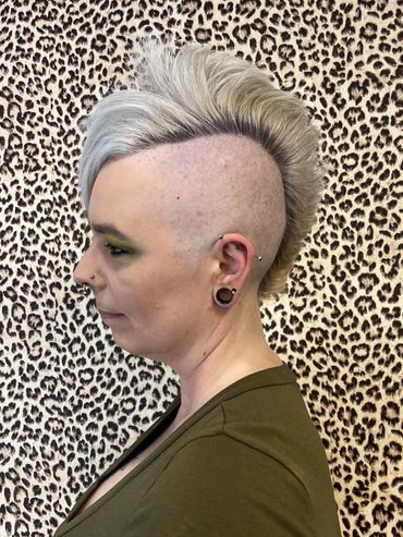 Person with a stylish mohawk and piercings in front of leopard print.