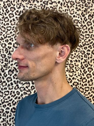 Side profile of a man with curly hair against a leopard print background.