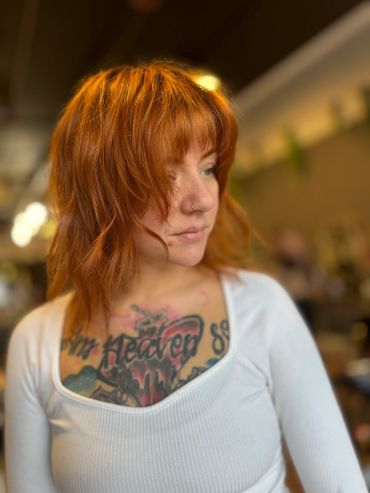 Thoughtful woman with red hair and chest tattoo.