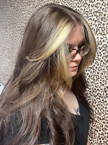 Woman with long, layered hair and glasses against leopard print wall.