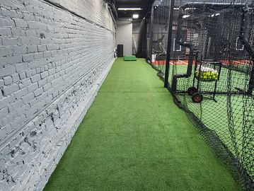 Indoor baseball practice area with artificial turf and batting cages.