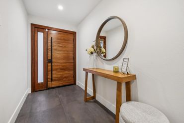 Minimalist entryway with wooden door, console table, round mirror, and decorative vase.