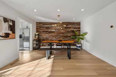 Modern dining area with wooden wall and table, black chairs, and a potted plant.