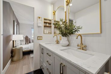 Modern bathroom with gold fixtures and double sinks beside a cozy bedroom.