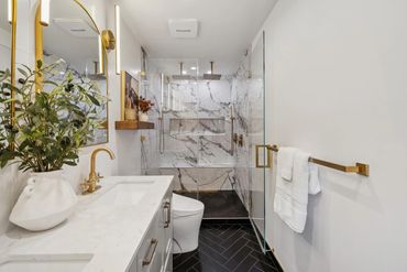 Modern bathroom with marble shower and gold fixtures.