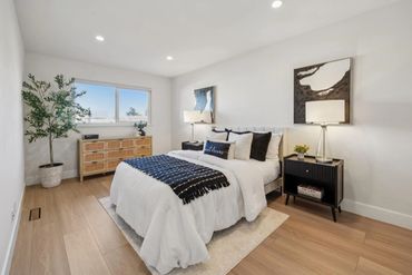 Modern bedroom with white bedding, wooden floor, and black accents.
