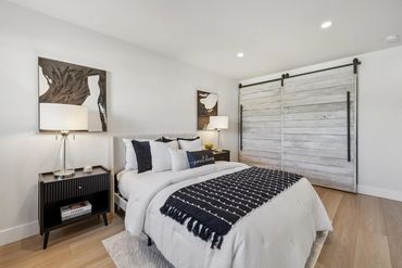 Modern bedroom with white bed linens, black accents, and sliding barn doors.
