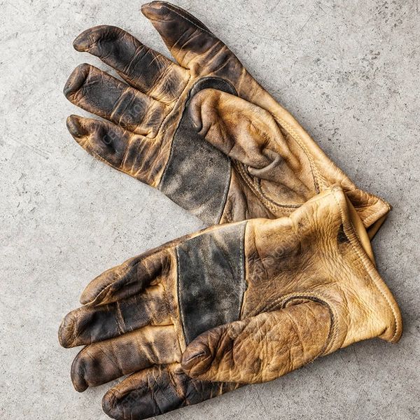 A pair of worn brown leather work gloves on a concrete surface.