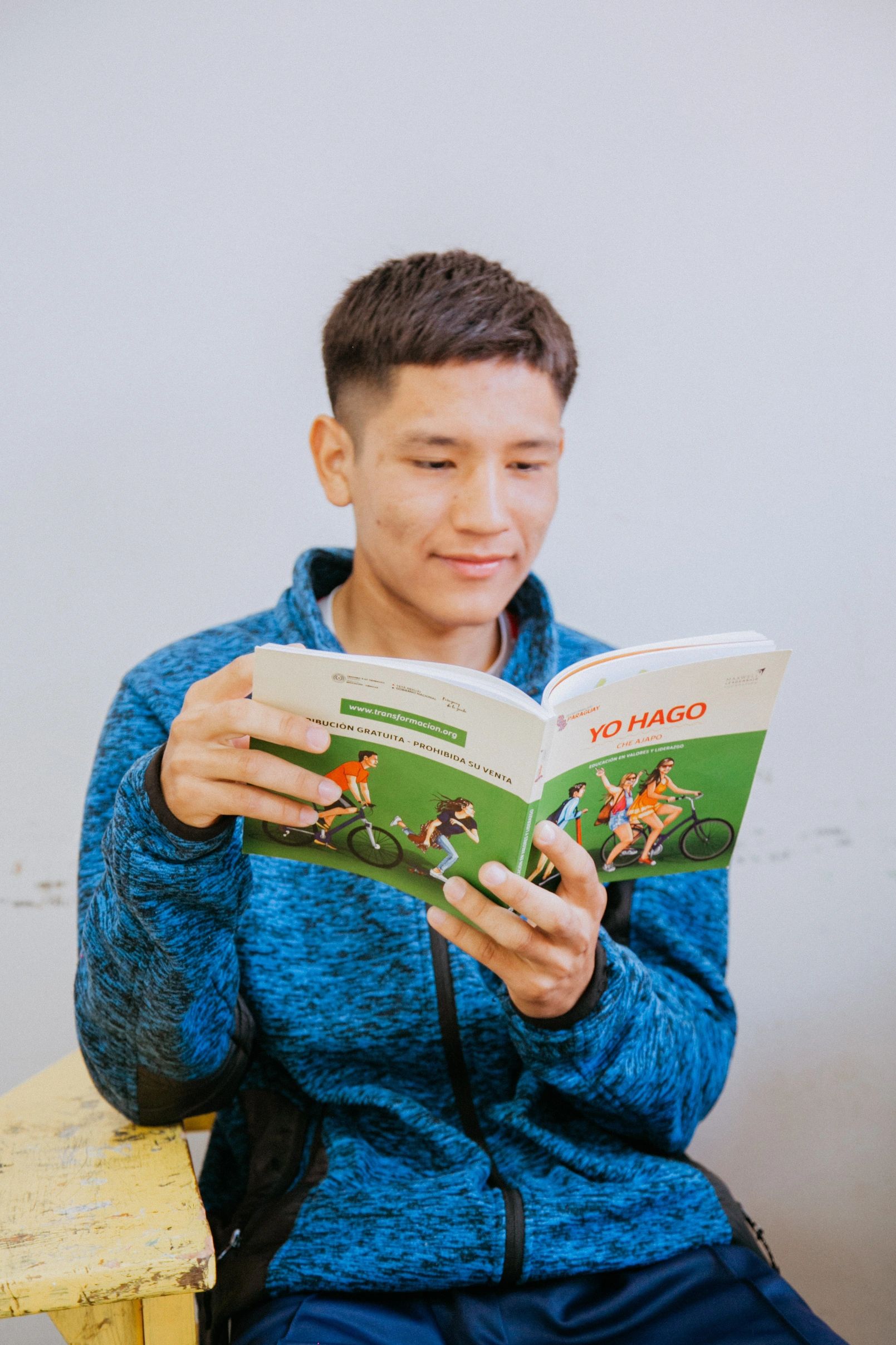 Young man in blue jacket reading a colorful book with illustrations.