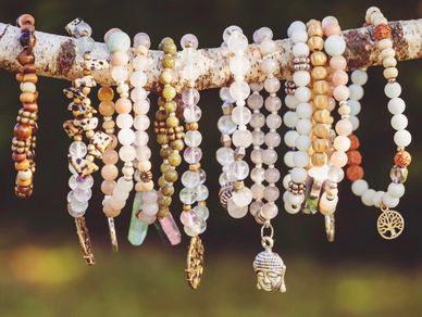Beaded bracelets with charms hanging on a branch outdoors.