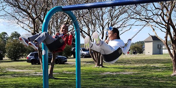 Two kids happily swinging on swings in a park.