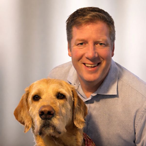 Mike smiling at the camera with his Labradoodle Loki in front both looking at the camera