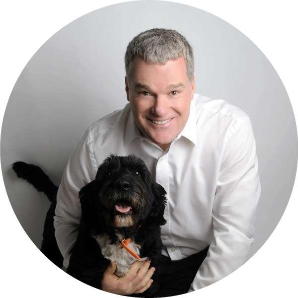Sean crouched down, hugging his Portuguese water dog Tux with his right arm looking into the camera.