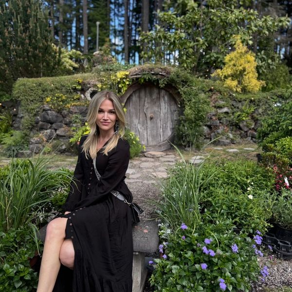 Woman in black dress sitting in front of a round wooden door.