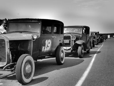 A lineup of vintage cars on a racetrack in black and white.