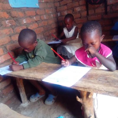 Children writing on papers in a rustic classroom.