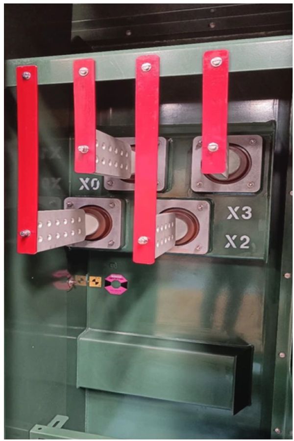Close-up of electrical busbars with red insulation inside a green panel.