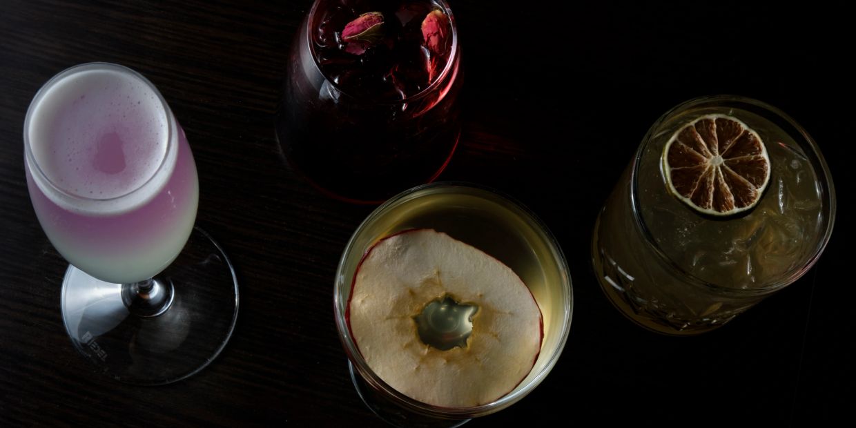 Four artisan cocktails with unique garnishes on a dark wooden surface.