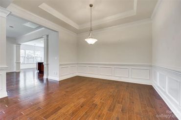 Empty room with dark hardwood floors, white walls, wainscoting, and a tray ceiling.
