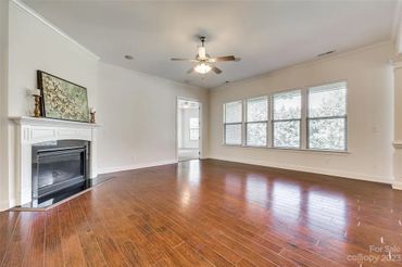 Empty living room with dark hardwood floors, white walls, a fireplace with a white mantel, and large windows.