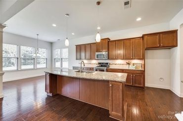 Kitchen with dark wood cabinets, a granite island with a sink, and pendant lights.
