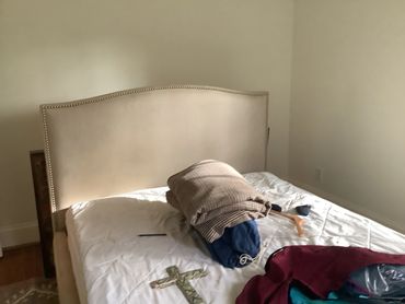 Close-up of a bed with a beige headboard and unorganized clothing.