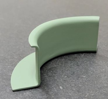 Curved light green plastic or rubber piece on a gray surface.