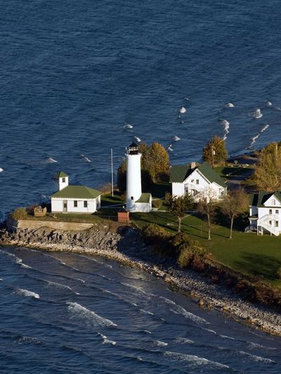 A lighthouse and houses on a rocky coastline with blue ocean waves.