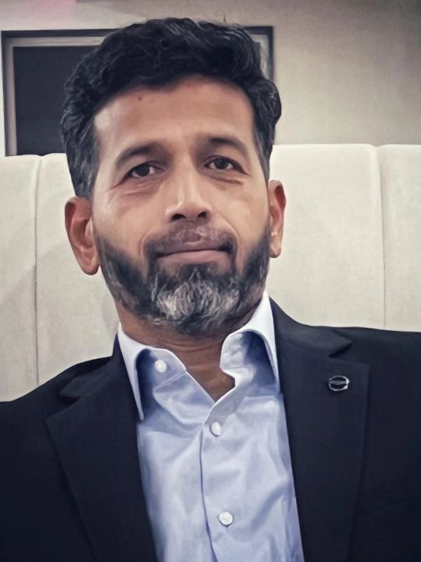 Man with beard in formal suit sitting indoors.