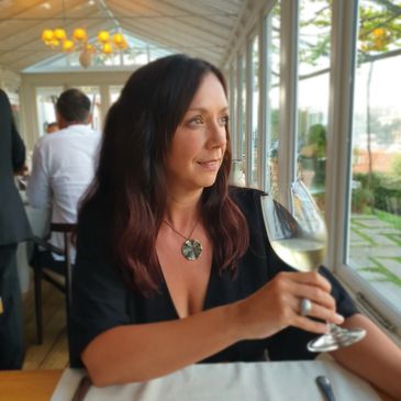 Woman with dark hair holding a glass of white wine in a bright restaurant.