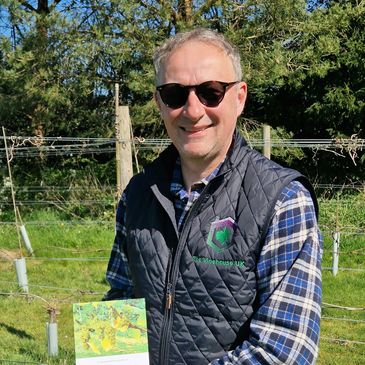 Man in vineyard holding a guidebook on running a micro vineyard.