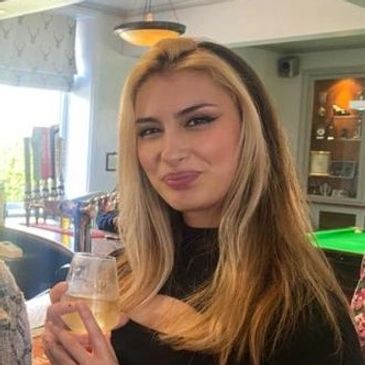 Woman with blonde hair holding a drink and smiling indoors.