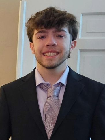 Young man smiling in a suit with a paisley tie indoors.