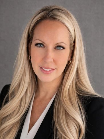Professional blonde woman with blue eyes posing against a gray background.