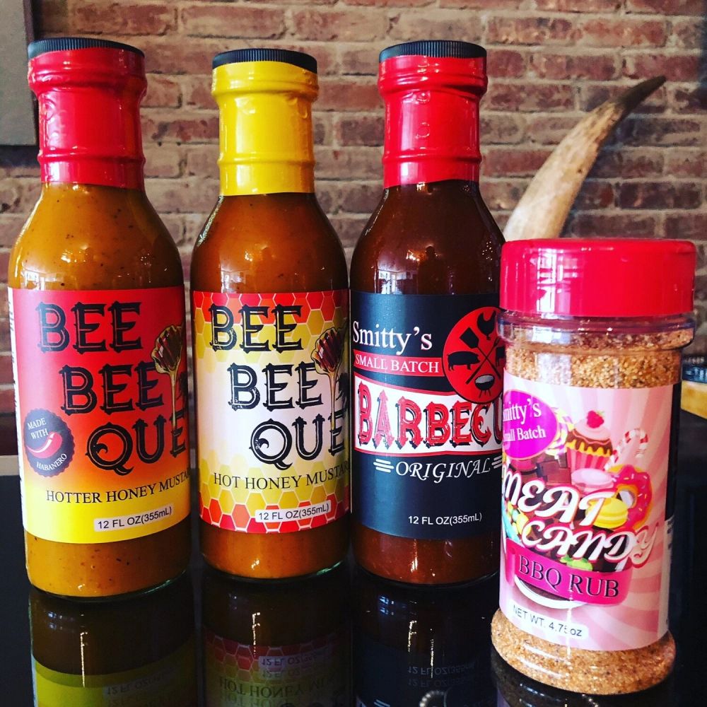 Four barbecue sauces and rubs lined up on a table with a brick wall background.