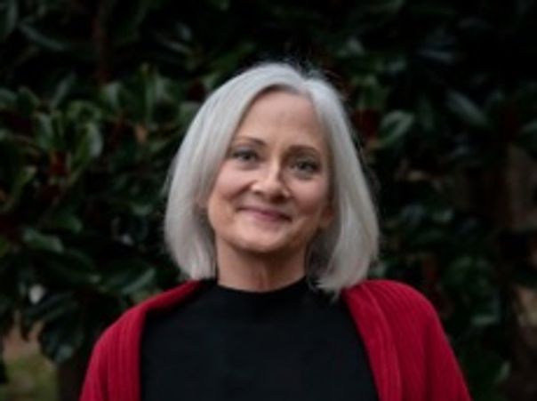 Smiling woman with white hair wearing a red cardigan and black top.
