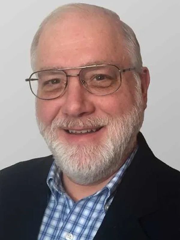 Smiling elderly man with glasses and white beard in formal attire.