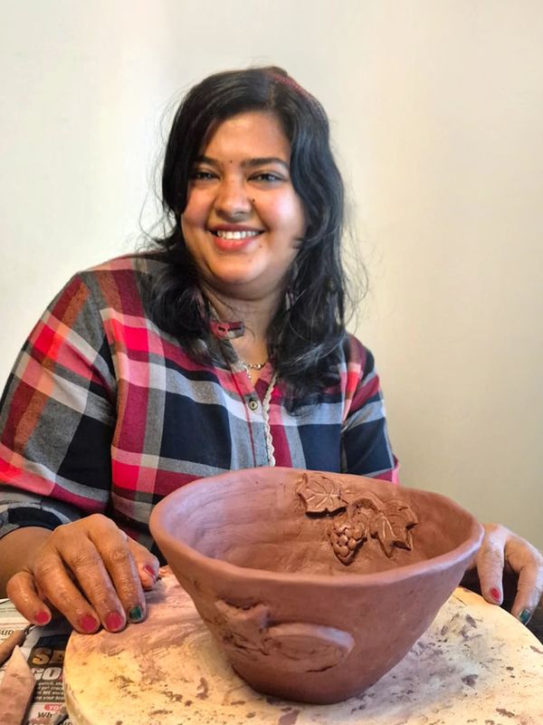 A woman proudly displays her handmade clay bowl with grapevine design.