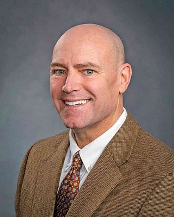 Smiling bald man in a brown suit and patterned tie.