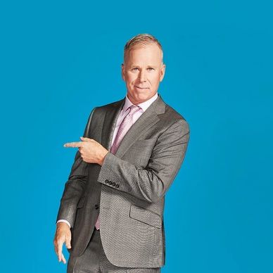 Man in gray suit pointing to his left against a blue background.