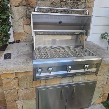 A stainless steel outdoor grill built into a stone countertop setup.