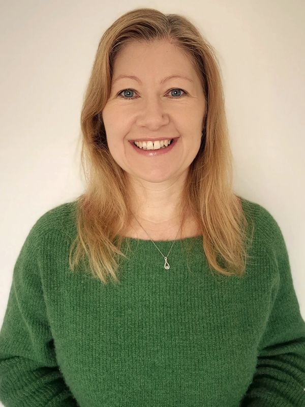 Image of Leah Clements from the waist up, smiling and wearing a green jumper.