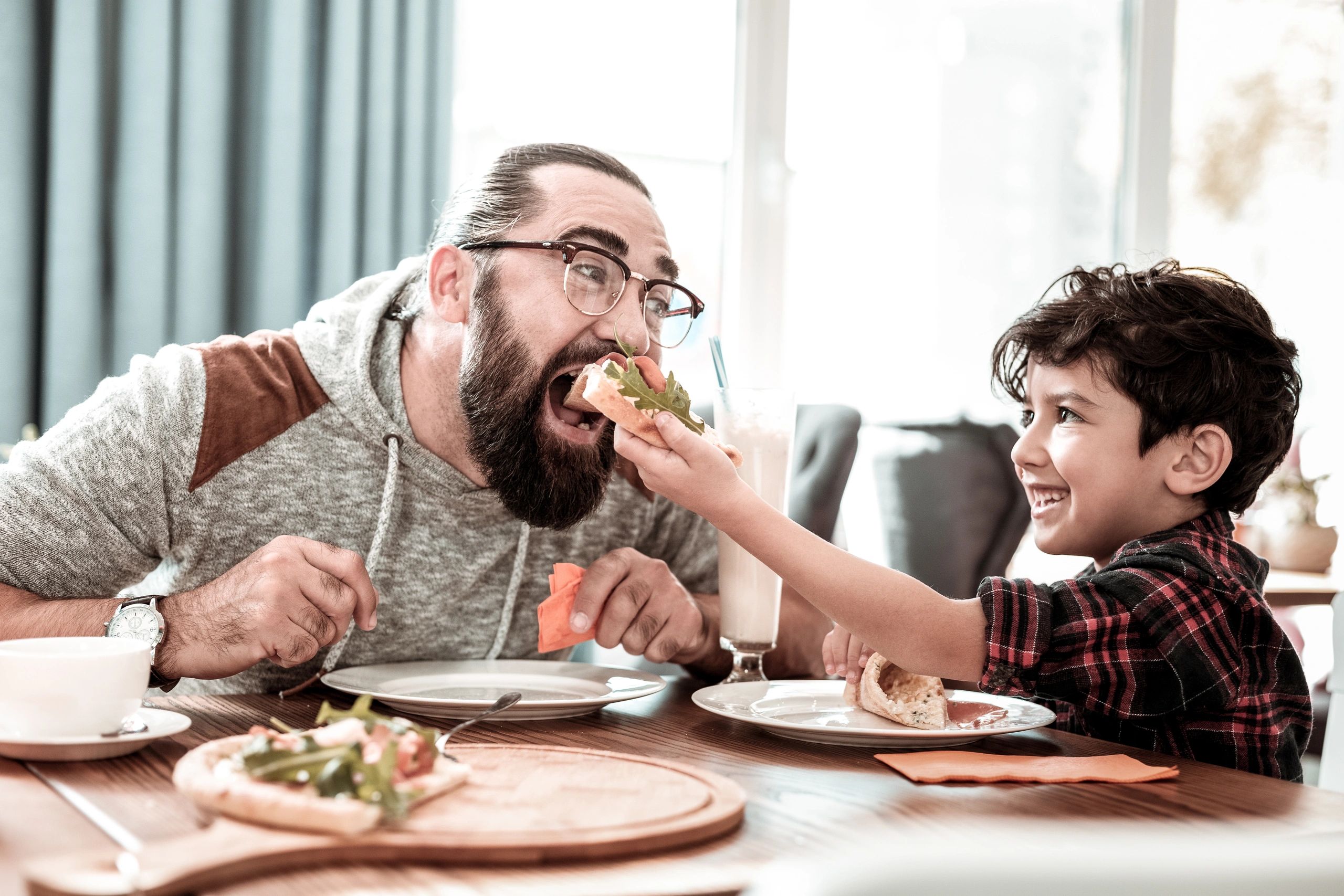 Child feeding a man pizza at a dining table.