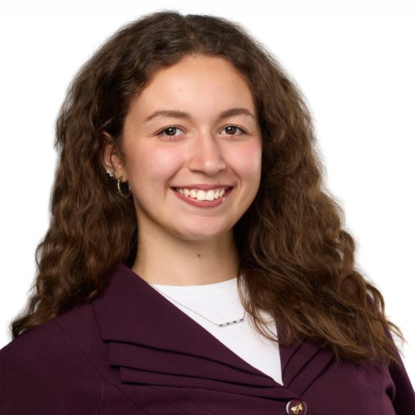 Smiling young woman with long curly hair wearing a dark purple blazer.