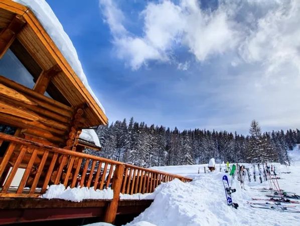 Log cabin, snow, skis, mountains, sky.