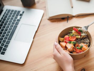 Person holding a bowl of healthy food near a laptop.